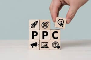 Hand placing a wooden block with a click icon on ppc cubes symbolizing pay per click advertising strategy and online marketing